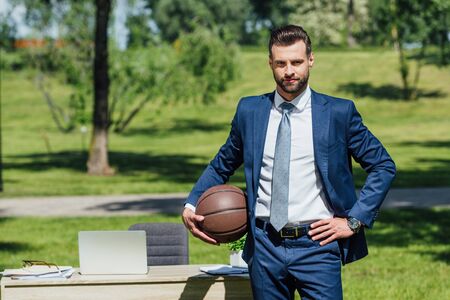 businessman standing neat table in park, holding basketball and looking at cameraの写真素材