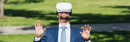 panoramic shot of businessman gesturing in park witn VR headset