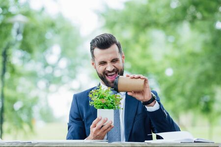 smiling handsome young businessman holding coffee to go and plantの写真素材