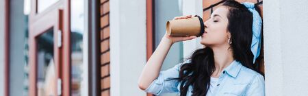 panoramic shot of attractive young woman drinking coffee to go while standing outsideの写真素材