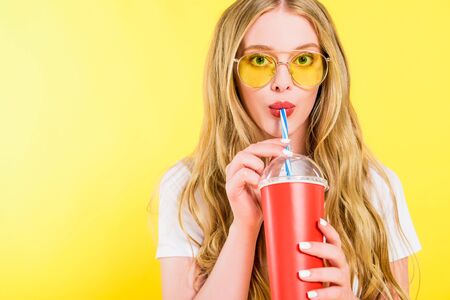 beautiful girl in sunglasses holding drink in disposable cup On yellowの写真素材