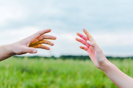 cropped view of man and woman with holi paint on hands gesturing near blue skyの写真素材