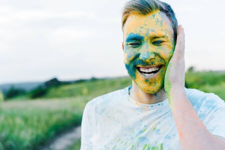happy young man with yellow and blue holi paints on face