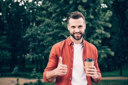 young man holding coffee to go and showing thumb upの写真素材