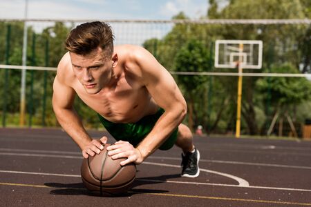 sexy shirtless sportsman doing push ups with ball at basketball court
