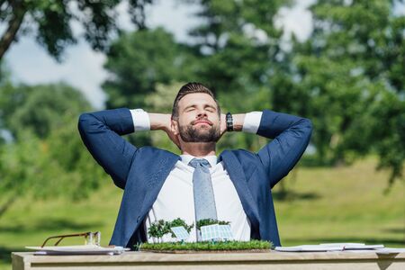 young businessman sitting at table with sun batteries layout and relaxing with hands behind head