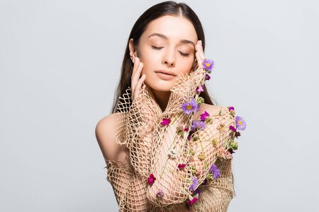 beautiful woman with closed eyes in mesh beige clothing with purple flowers touching face isolated on grey with copy spaceの写真素材