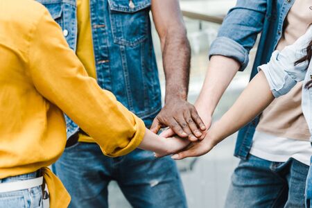 cropped view of multicultural friends putting hands together
