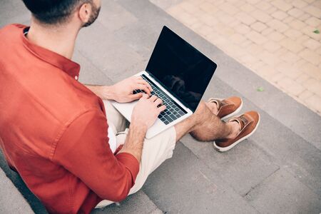cropped view of young man sitting on stone stairs and using laptopの写真素材