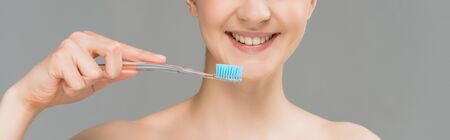 panoramic shot of happy naked woman holding toothbrush near teeth isolated on grey