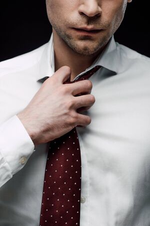 partial view of serious businessman touching tie isolated on blackの写真素材