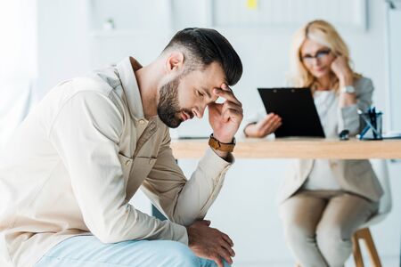 selective focus of frustrated man sitting near blonde recruiterの写真素材