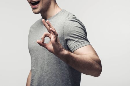 cropped view of young man showing ok gesture isolated on grey, human emotion and expression conceptの写真素材