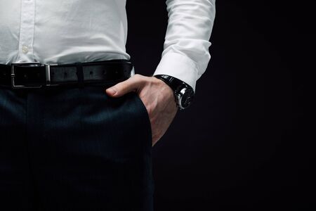 partial view of businessman holding hand in pocket isolated on black