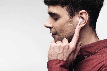 pensive man with closed eyes listening music in earphones isolated on grey