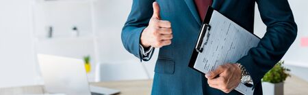 panoramic shot of recruiter standing and holding clipboard with resume letters while showing thumb...