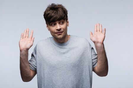 smiling man showing give up gesture and looking away isolated on grey, human emotion and expression...