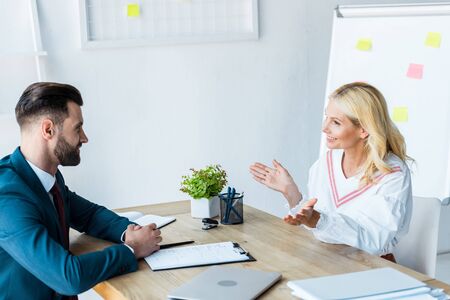 cheerful and bearded recruiter looking at woman gesturing in officeの写真素材