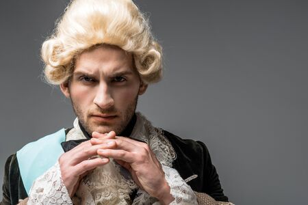 serious victorian gentleman in wig looking at camera isolated on greyの写真素材