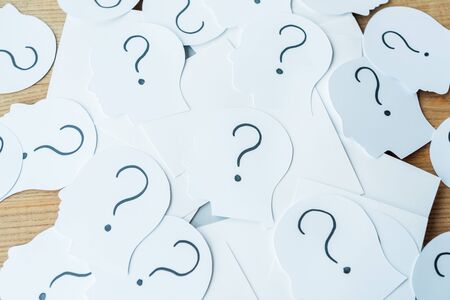 question marks on paper with human heads on wooden table