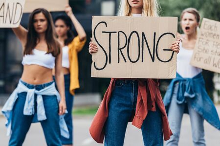 cropped view of feminist holding placard with inscription strong near women on streetの写真素材