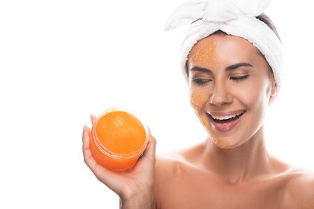 smiling young woman in cosmetic hair band with scrub on face holding container isolated on whiteの写真素材