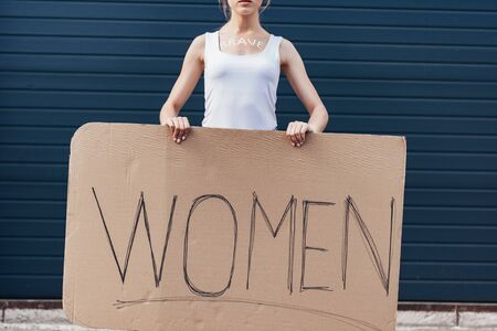 cropped view of feminist with word brave on body holding placard with inscription women on streetの写真素材