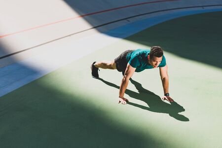 mixed race sportsman pressing-up at stadium in light place