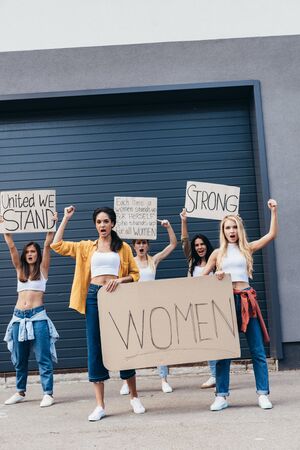 full length view of screaming multiethnic feminists holding placards with slogans on streetの写真素材