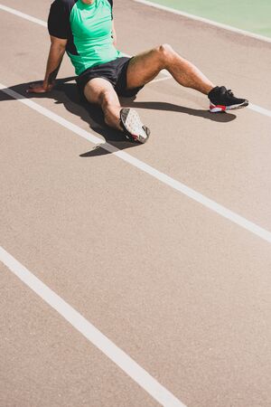 cropped view of tired sportsman sitting at stadiumの写真素材