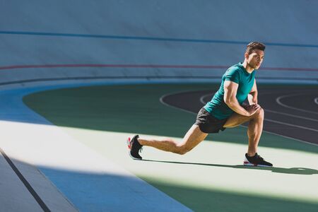 mixed race sportsman warming up at stadium in light place