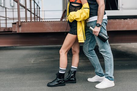 cropped view of man in jeans holding bottle and woman in yellow jacket