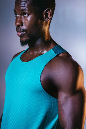 confident, athletic african american sportsman looking away on grey and blue gradient background with lightingの写真素材