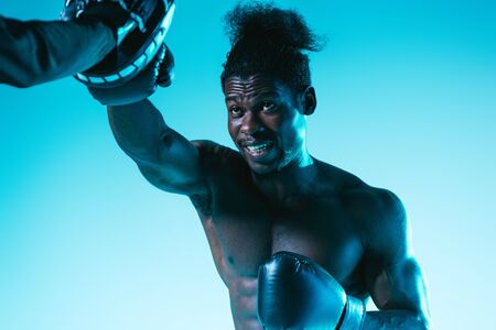 muscular african american boxer working out with trainer on blue backgroundの写真素材
