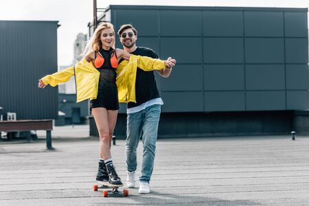 attractive and smiling woman skateboarding and man in glasses hugging herの写真素材