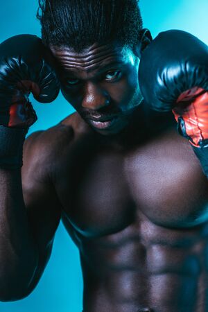 confident african american sportsman in boxing gloves looking at camera on blue backgroundの写真素材