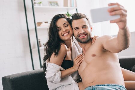 handsome man and sexy woman in shirt and bra smiling and taking selfieの写真素材