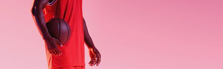 partial view of african american basketball player holding ball isolated on pink, panoramic shotの写真素材