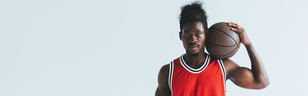 panoramic shot of african american basketball player holding ball and looking at camera isolated on greyの写真素材