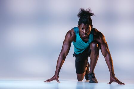 african american sportsman standing in start position and looking at camera on grey background with lightingの写真素材