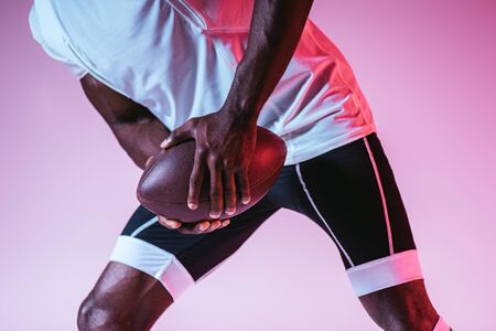 partial view of african american sportsman playing american football on purple background with...