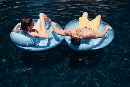 young couple sunbathing while relaxing on swim rings in swimming poolの写真素材