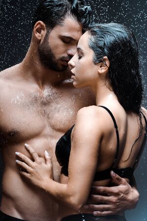 handsome and shirtless man hugging sexy girl under raindrops on blackの写真素材