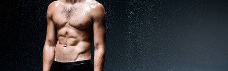 panoramic shot of shirtless sexy man standing under raindrops on blackの写真素材