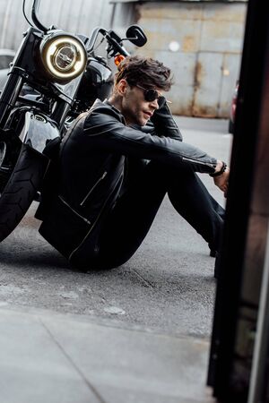 handsome young motorcyclist sitting on ground near black motorcycle with luminous lampの写真素材
