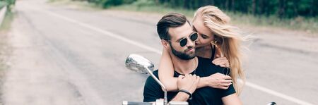 young couple of bikers closely embracing on black motorcycle, panoramic shotの写真素材