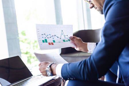 cropped view of man in formal wear looking at papers with charts and graphsの写真素材