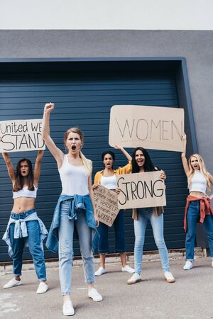 full length view of screaming multiethnic feminists holding placards with slogans on streetの写真素材