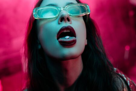 beautiful girl in sunglasses with lsd on tongue in nightclubの写真素材