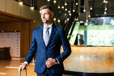 handsome and confident businessman in suit looking away in hotel